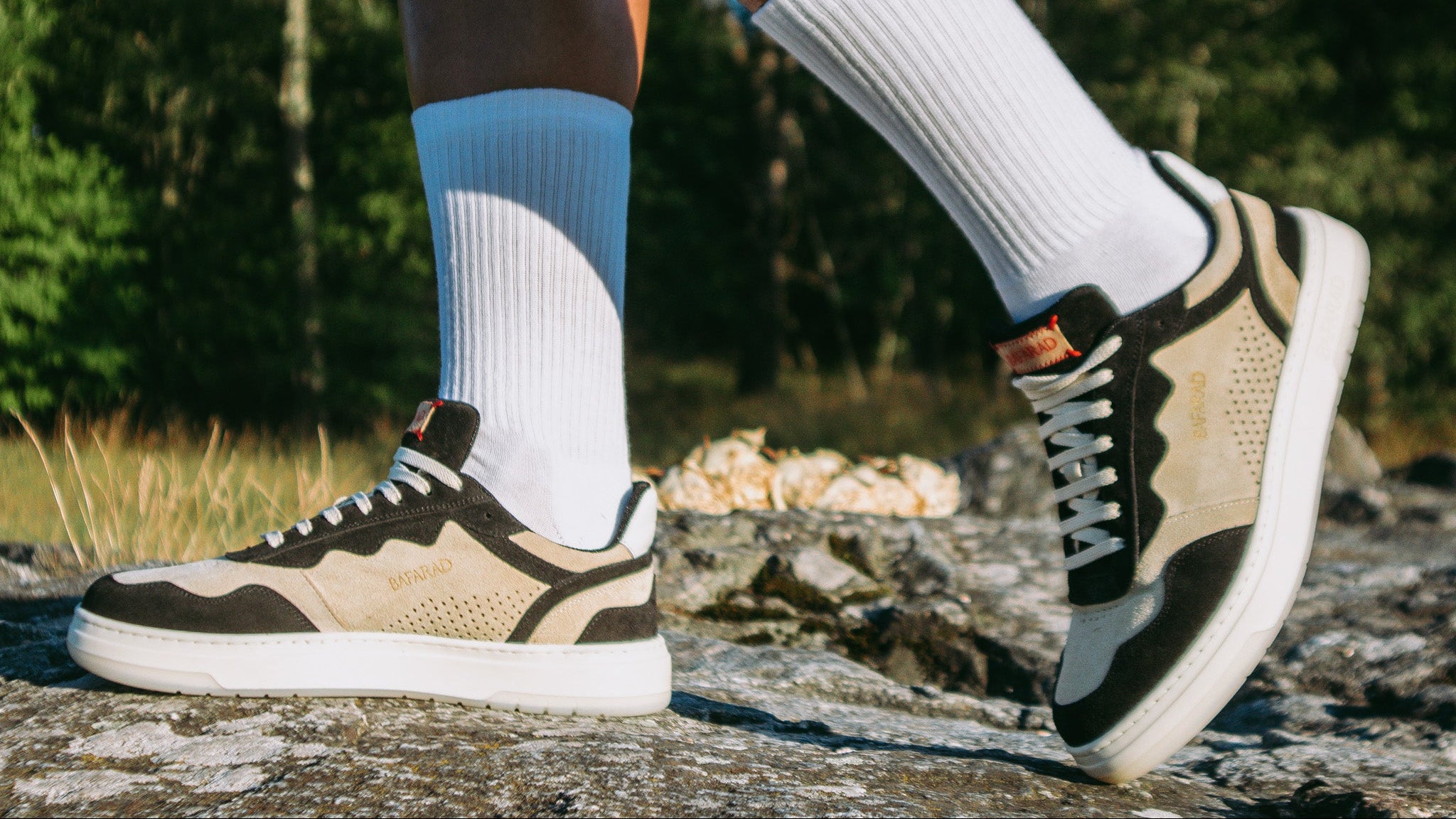 Person wearing beige sneakers with black accents and white socks in a natural setting.