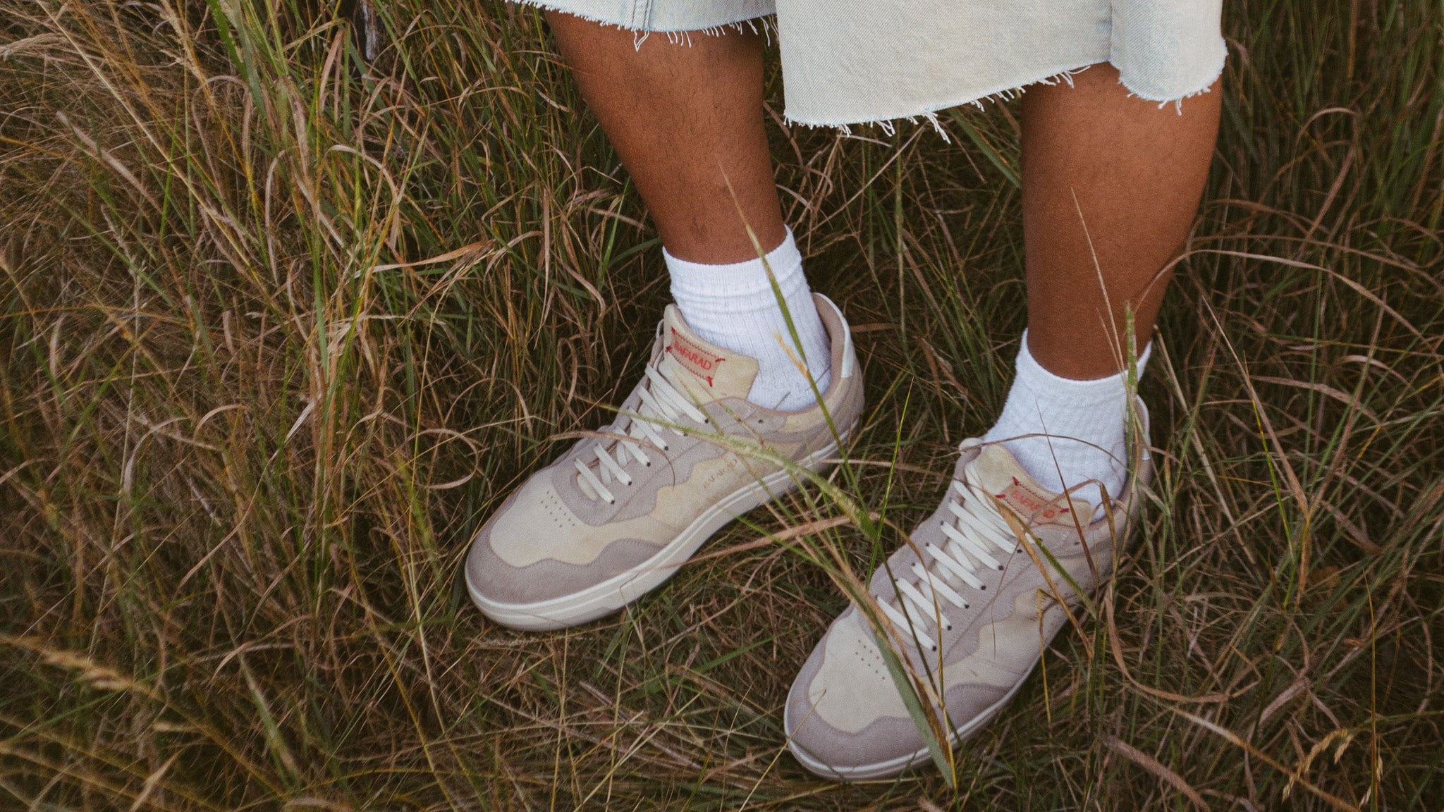 Person wearing light-colored sneakers and white socks standing in tall grass.