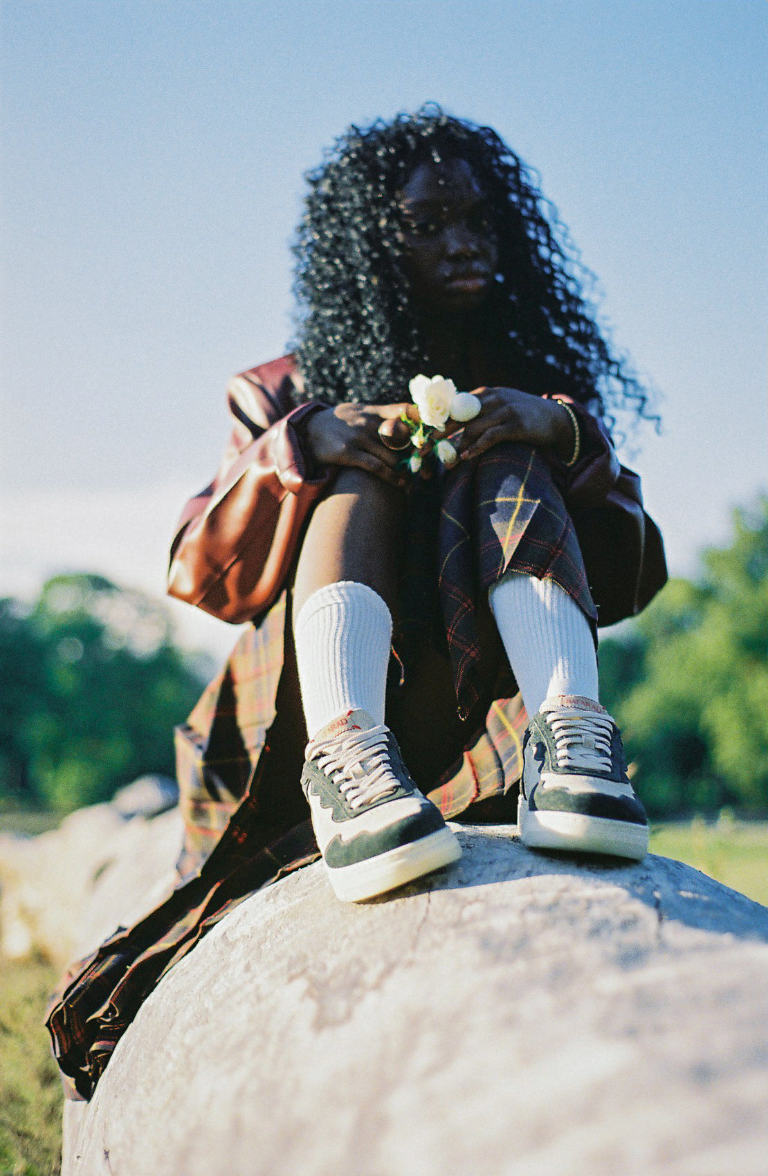 Person sitting on a rock outdoors with a clear blue sky and wearing teranga green shoes