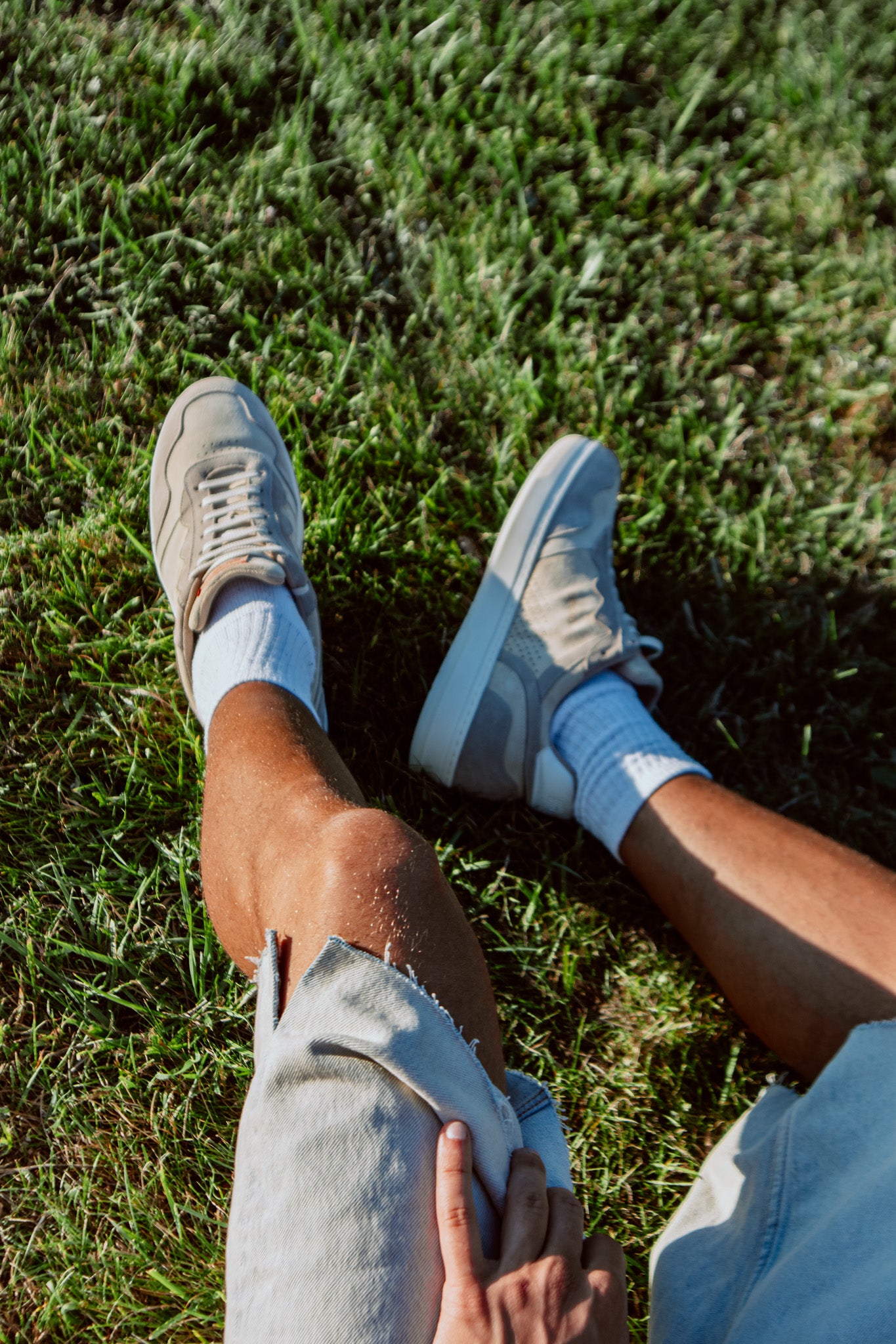 Person wearing light grey sneakers and socks sitting on grass