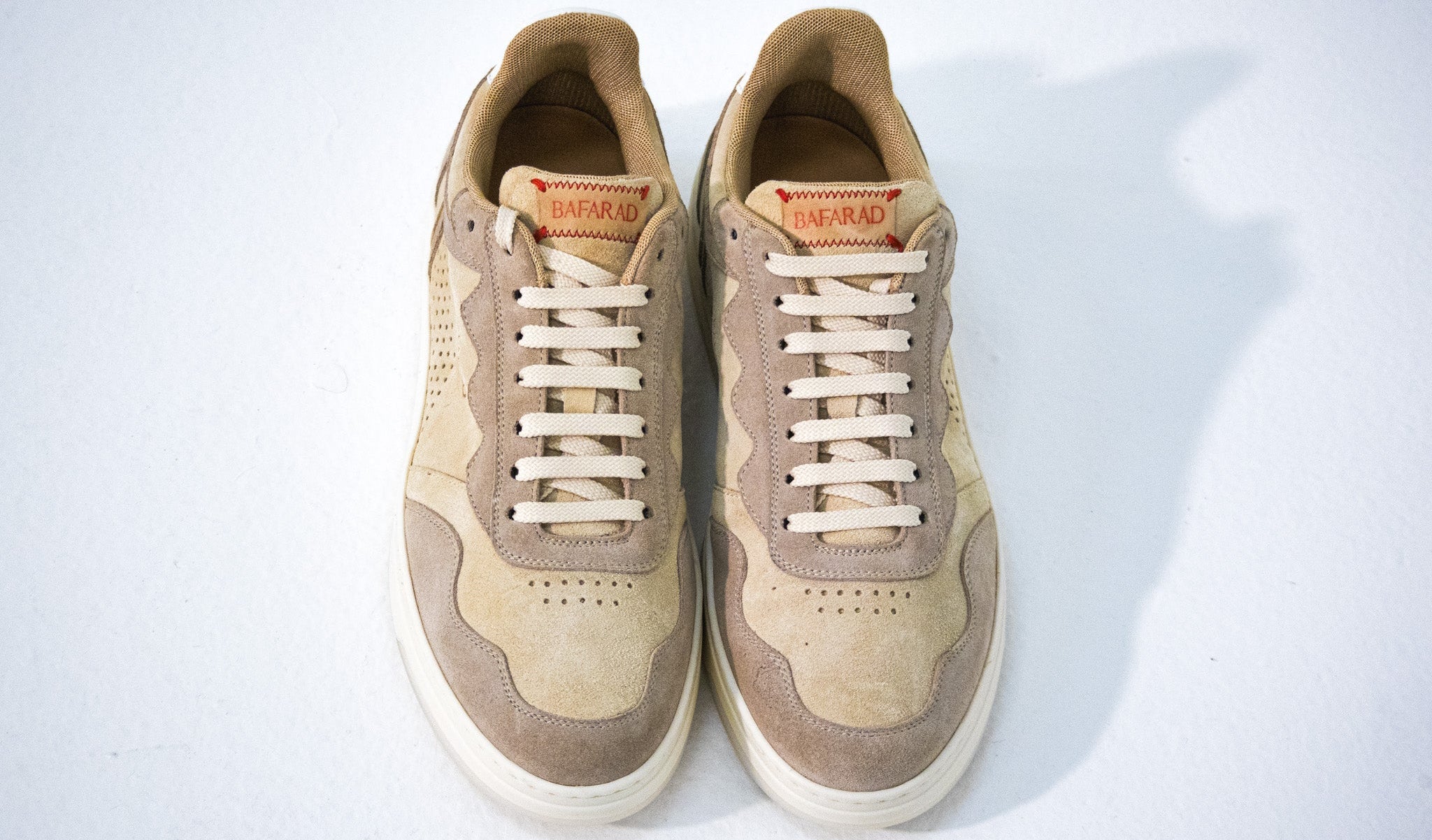 Pair of beige sneakers with white laces on a light gray background