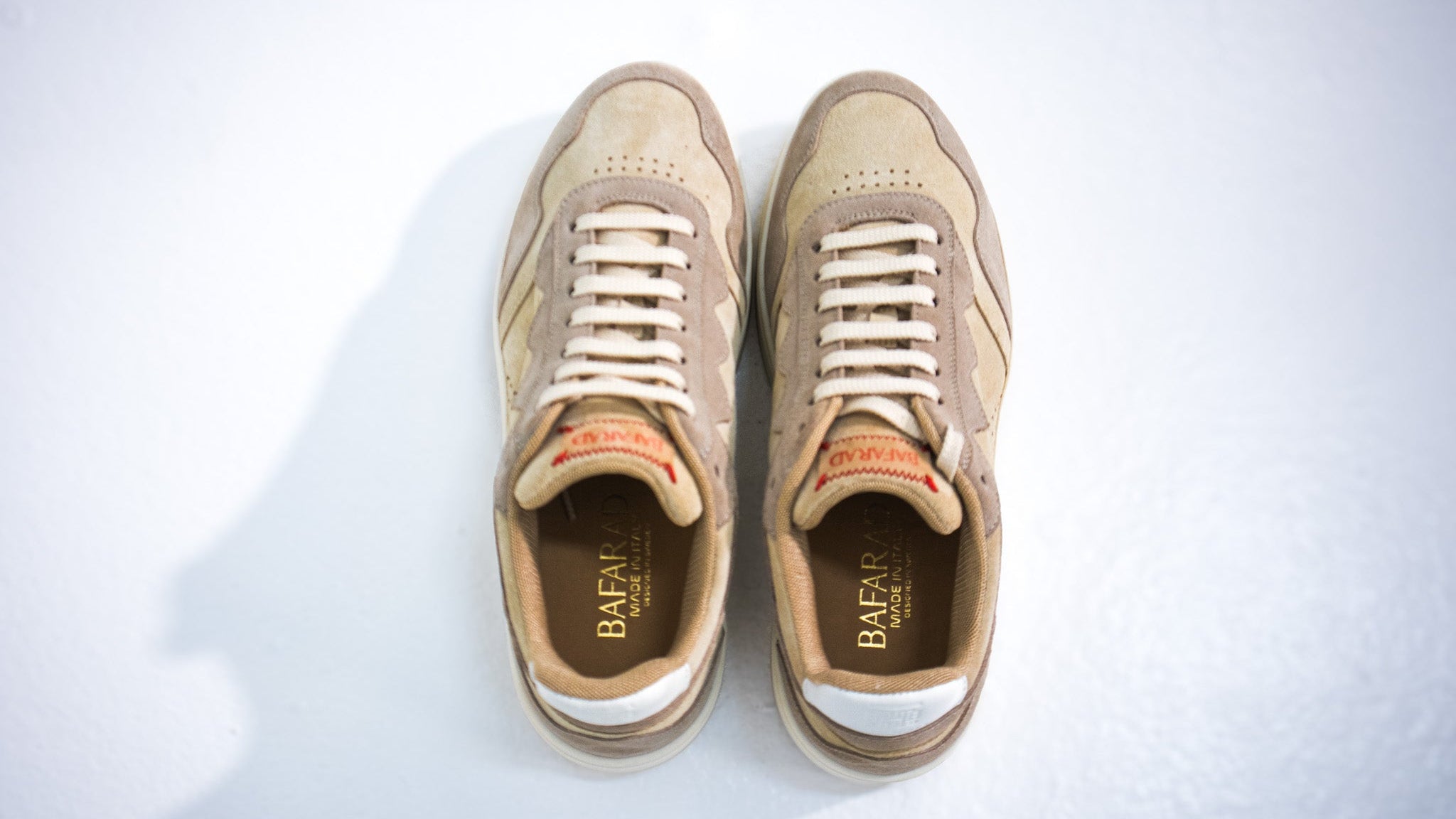 Pair of beige sneakers with white laces on a light gray background